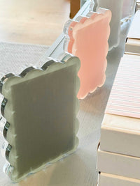 norsu Studio Scalloped Magnetic Photo Frame in sage and pink with scalloped edges and clear acrylic finish on a table near stacked boxes