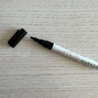 Black liquid chalk marker with fine tip and removable cap on wooden surface