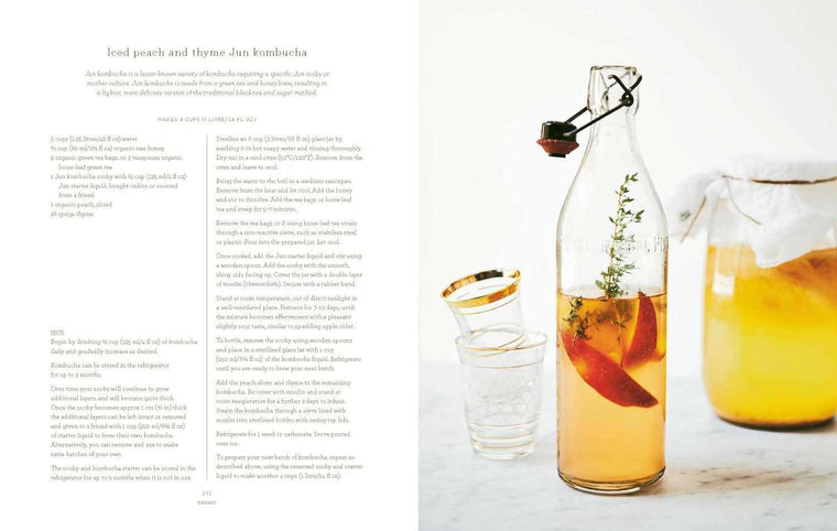 Glass bottle of iced peach and thyme Jun kombucha with gold rimmed glass and jar of kombucha on marble surface