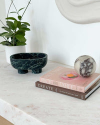 Stack of cookbooks including Rice Table by Su Scott with a decorative marble object and potted plant on a marble surface