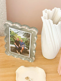 norsu Studio scalloped magnetic photo frame with acrylic finish displaying a portrait photo on a wooden surface next to a white decorative vase