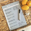 Sky blue magnet meal planner on woven surface with marker and lemons for fridge organization