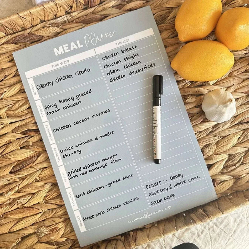 Sky blue magnet meal planner on woven surface with marker and lemons for fridge organization
