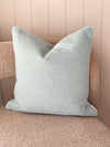 norsu Studio Cushion in powder blue boucle fabric with white leather piping on a textured beige chair