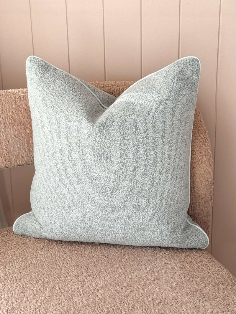 norsu Studio Cushion in powder blue boucle fabric with white leather piping on a textured beige chair