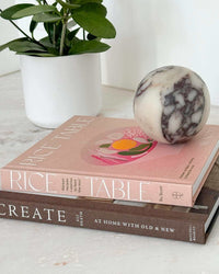 Rice Table by Su Scott cookbook on Korean Fried Chicken and modern Korean recipes stacked on a table with a plant and marble sphere decor.