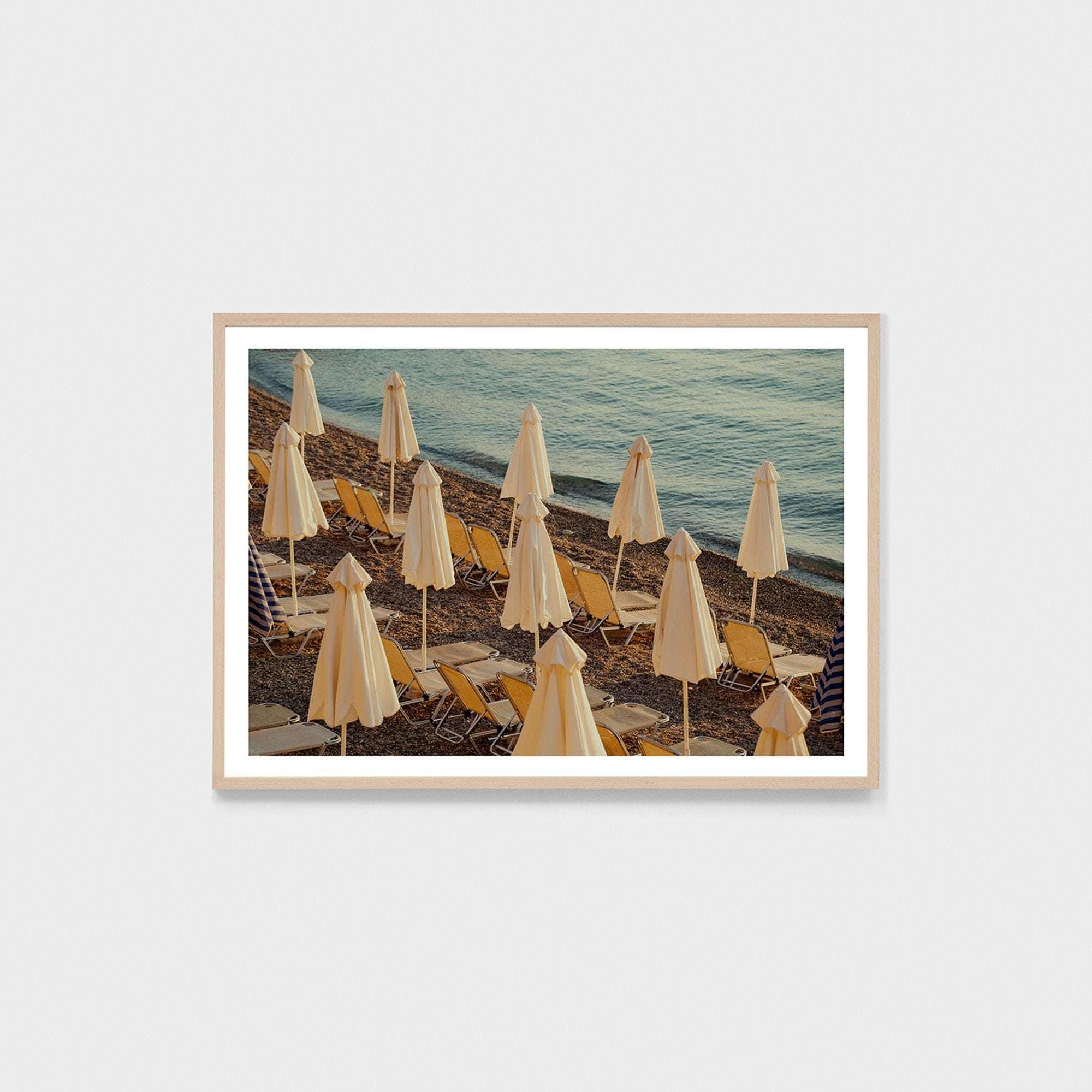 Framed photographic print of a serene Corfu sunrise with closed beach umbrellas and lounge chairs by the sea, part of the Middle of Nowhere collection.