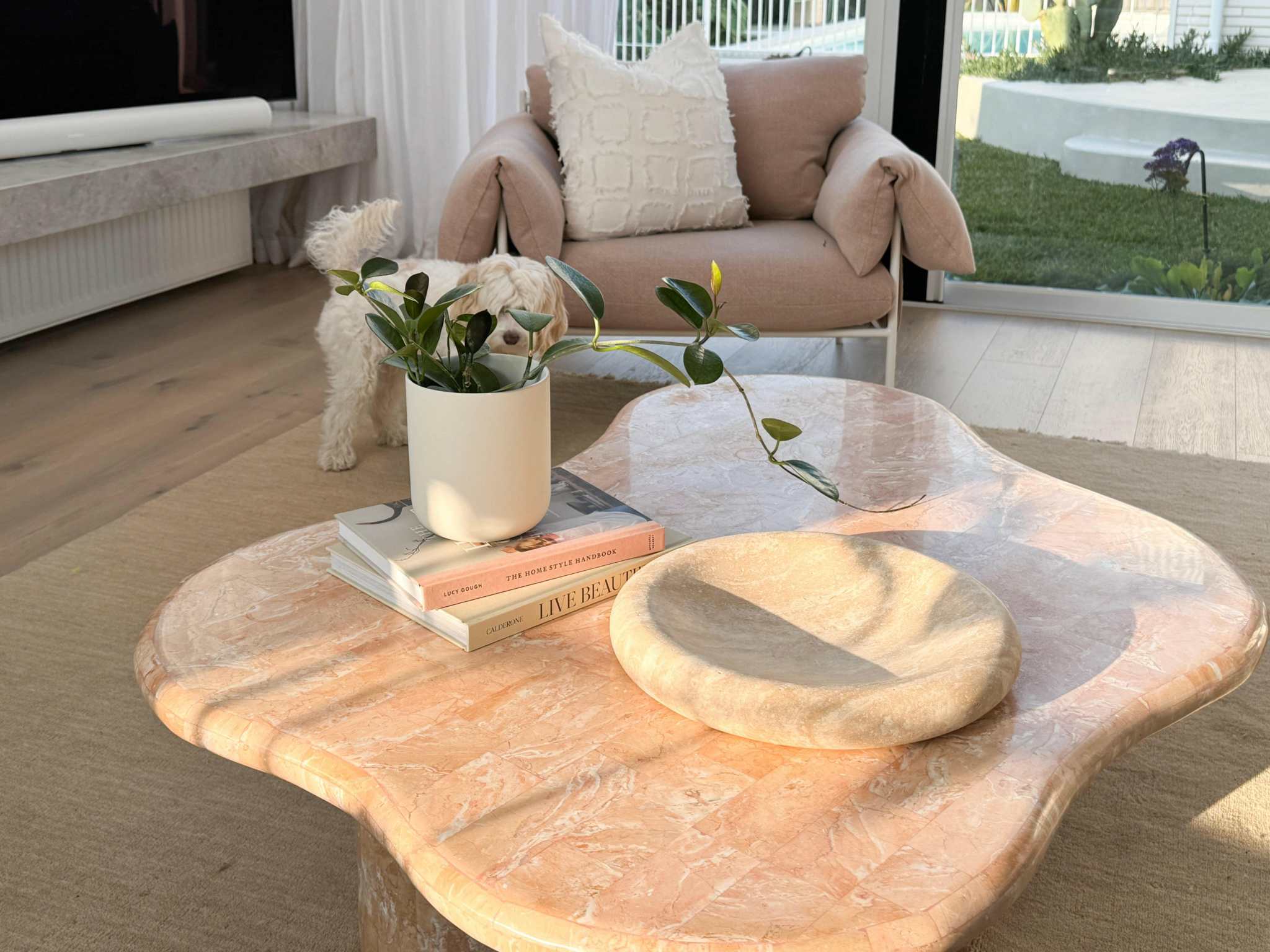 Modern beige marble coffee table styled with books, a white vase with greenery, and minimal decor in a bright living room setting