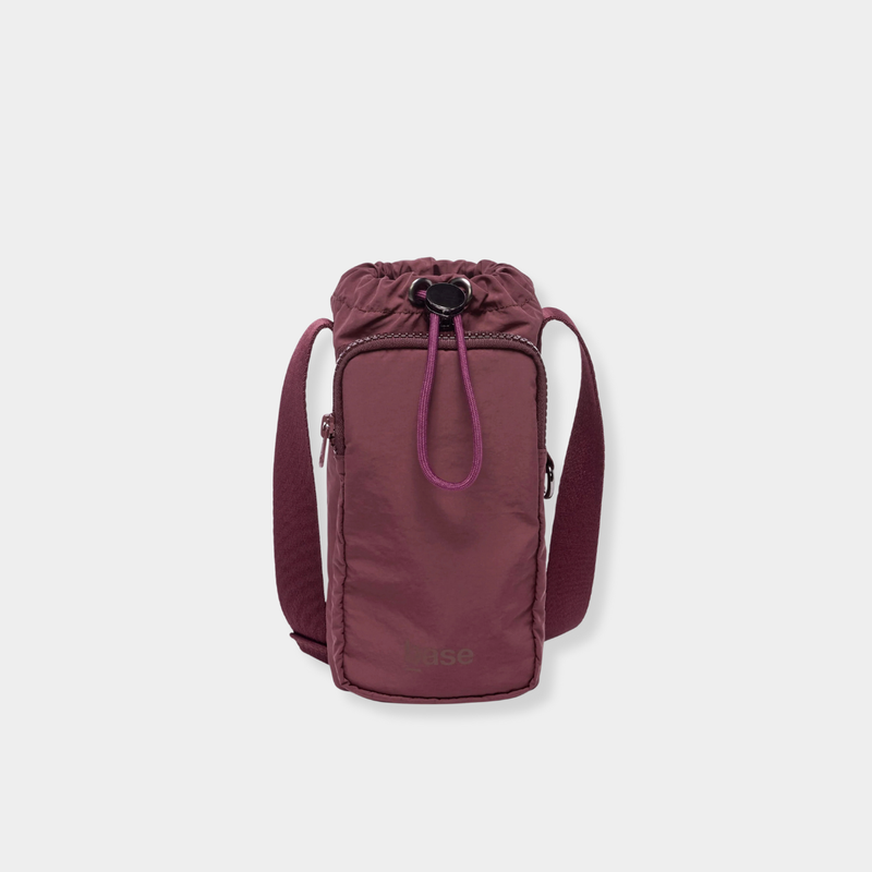 Base Supply Bottle Sling crossbody in burgundy, waterproof, adjustable strap, with front zipped pocket and drawstring top closure.