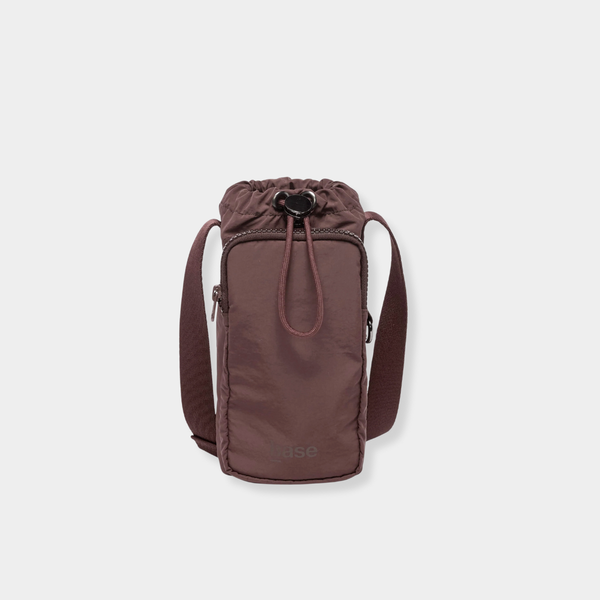 Base Supply Bottle Sling crossbody in chocolate brown, waterproof with adjustable strap and front zip pocket for phone.