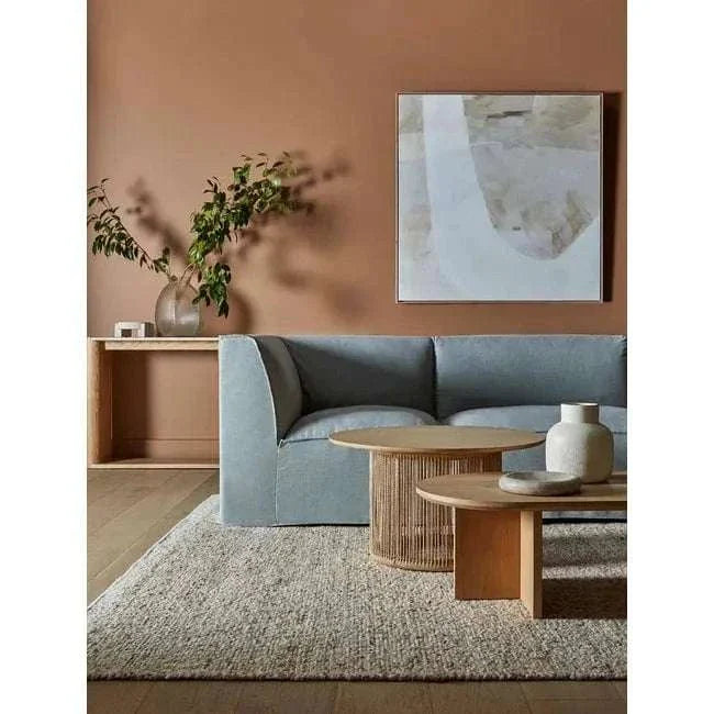 GlobeWest Tepih Maren Rug in stone color, hand-woven 100% wool, placed in a modern living room setting with blue sofa and wooden tables