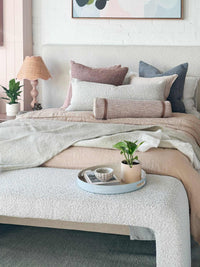 Baya Sorrento Throw in off-white with soft brushed wool texture and feathered fringe on a bed with decorative pillows and neutral decor