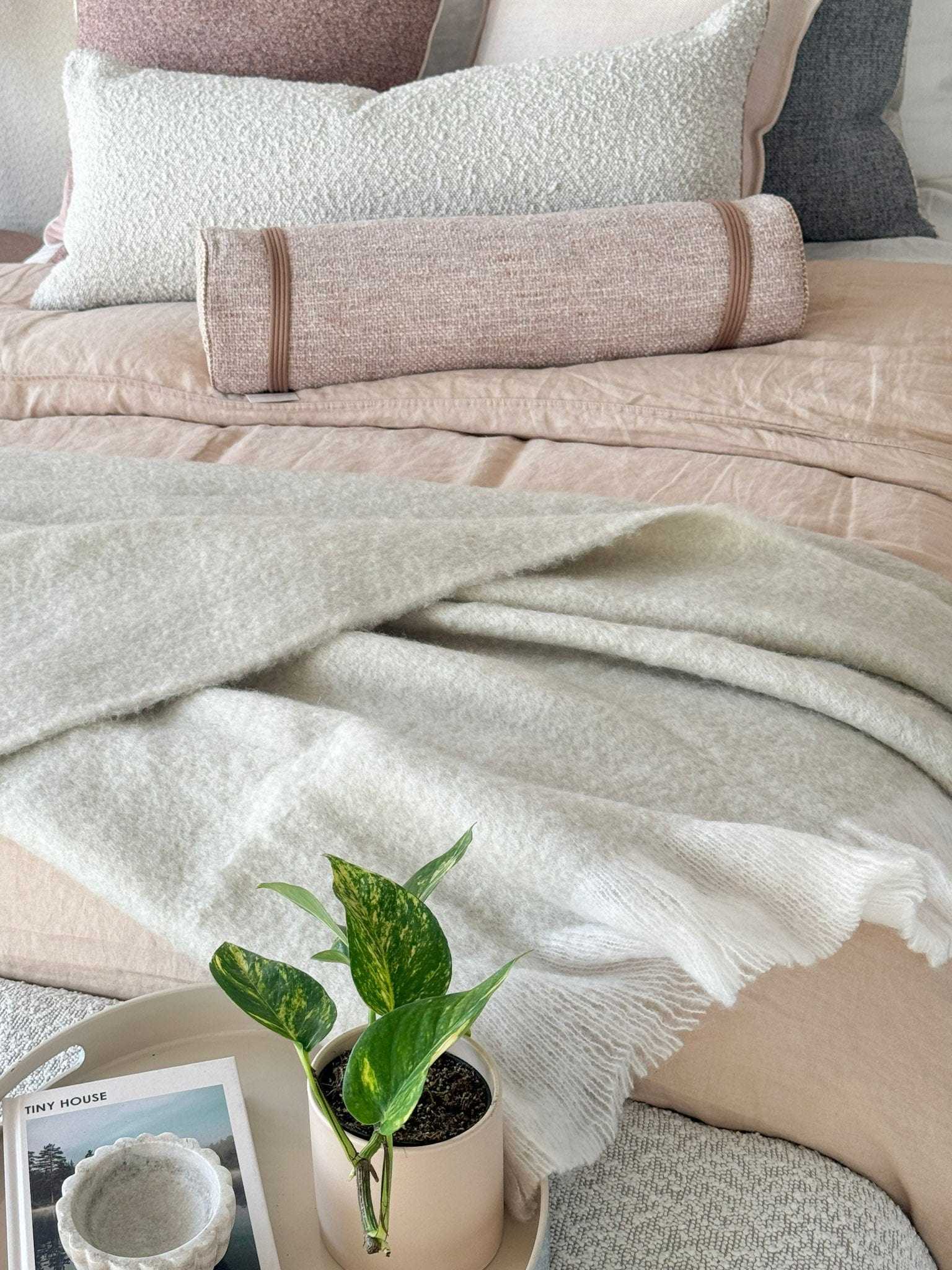 Off-white Baya Sorrento Throw with feathered fringe on bed with neutral bedding and green plant.
