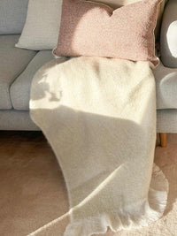 Baya Sorrento Throw in off white with soft brushed wool texture and feathered fringe draped on a sofa