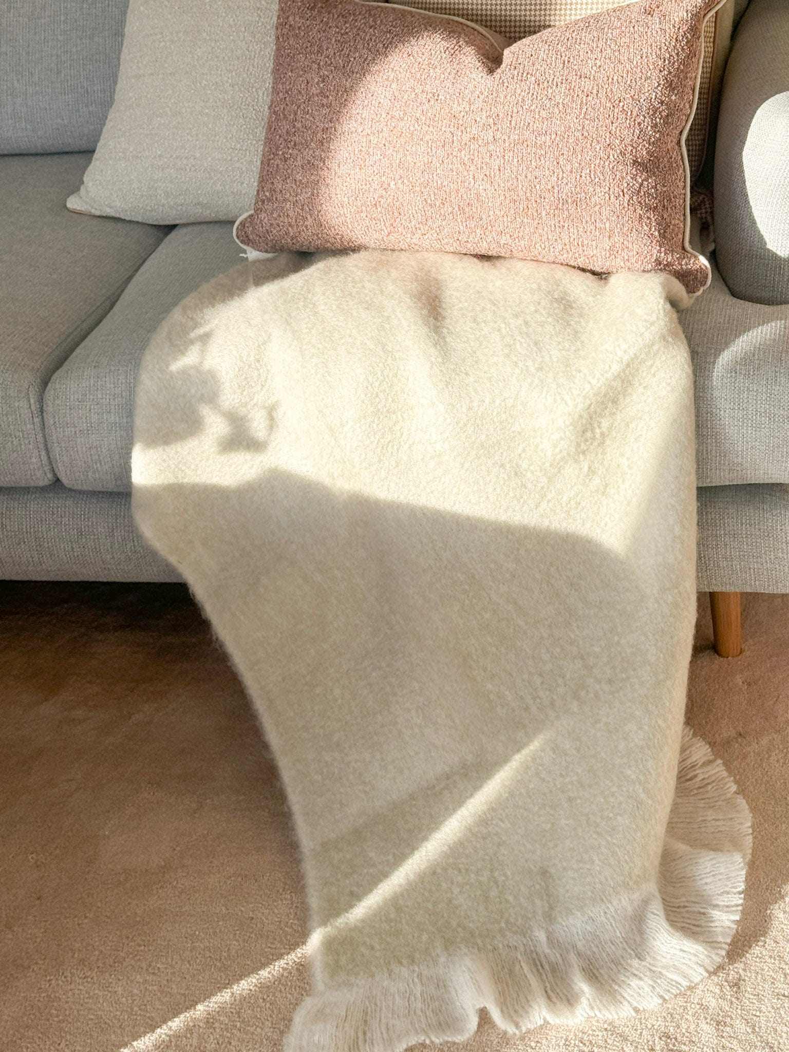 Baya Sorrento Throw in off white with soft brushed wool texture and feathered fringe draped on a sofa