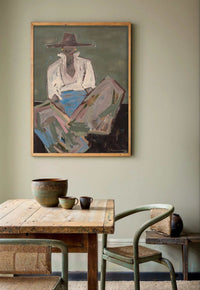 Oak framed Marcia Priestley 'Chaps 3' canvas print hanging above rustic wooden dining table with ceramic cups and green chair
