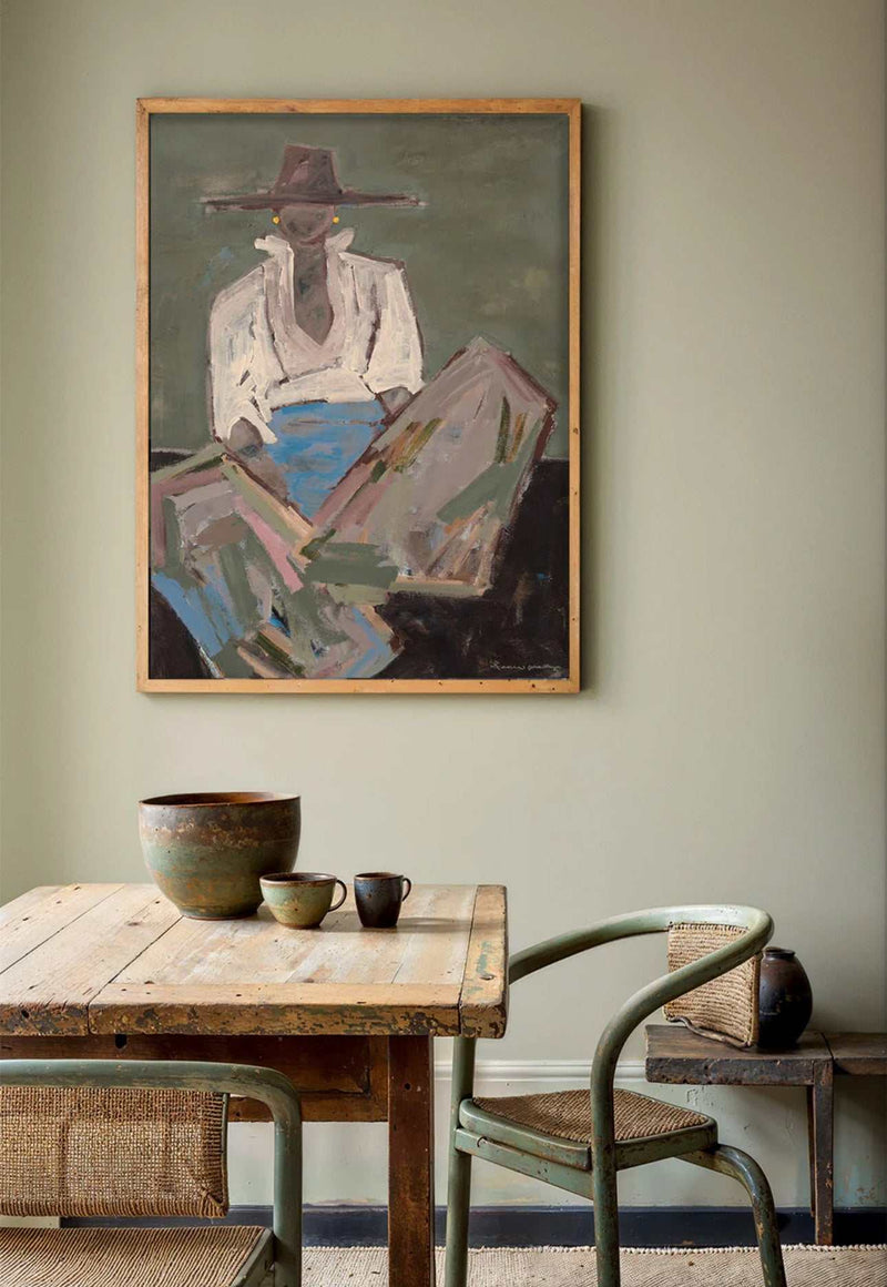 Oak framed Marcia Priestley 'Chaps 3' canvas print hanging above rustic wooden dining table with ceramic cups and green chair