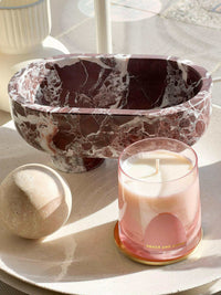 CoTheory Marble Footed Oval Tray in Rosso Levanto marble with sculptural design on table next to candle and decorative sphere