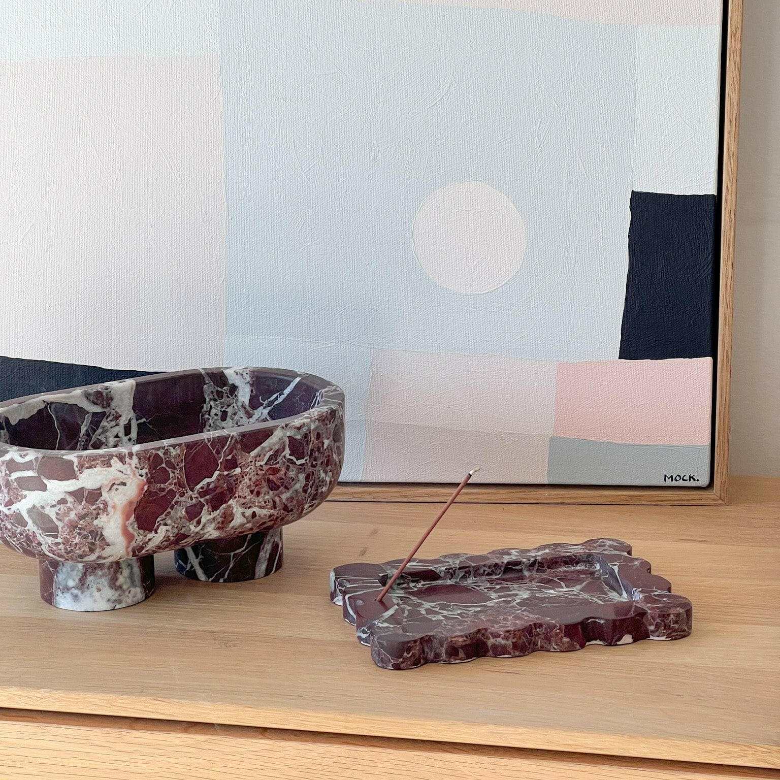CoTheory Rosso Levanto marble tray and small scalloped incense holder on wooden surface with abstract artwork background