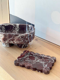 CoTheory Marble Footed Oval Tray in Rosso Levanto marble with sculptural design and organic form placed on wooden surface