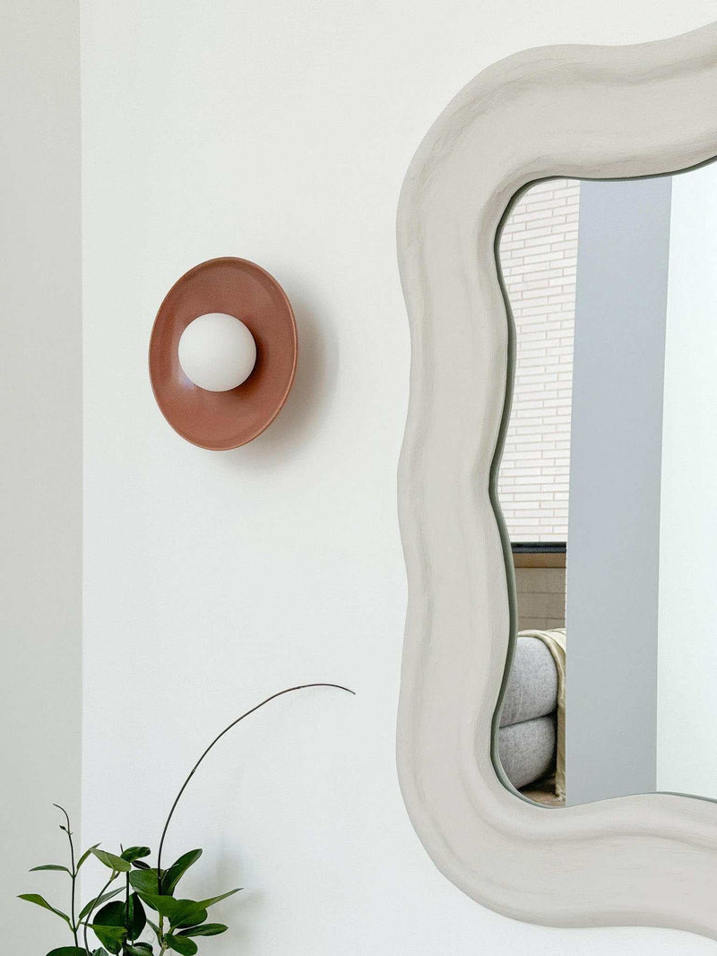 norsu x Robert Gordon dusty rose ceramic dish wall sconce with LED globe next to decorative mirror