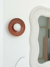 norsu x Robert Gordon Dusty Rose ceramic dish wall sconce with ball light mounted on white wall next to decorative mirror