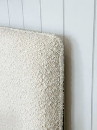 Close-up of ivory norsu Cabin Bedhead with textured Ovis boucle fabric and self-piped trim against white wall