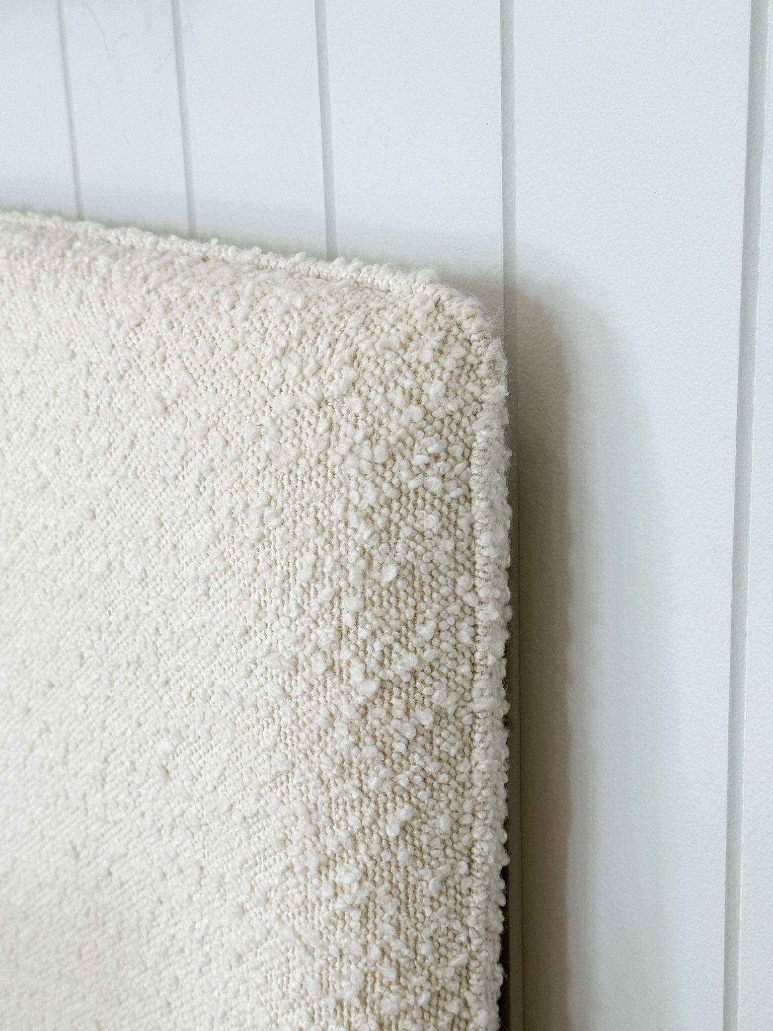 Close-up of ivory norsu Cabin Bedhead with textured Ovis boucle fabric and self-piped trim against white wall