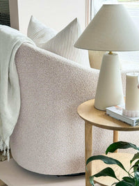 Blush boucle norsu Studio Swivel Chair with feather cushion in cozy living room corner next to wooden side table and lamp