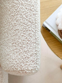 Close-up of blush boucle fabric texture on norsu Studio Swivel Chair armrest next to a wooden table with books and decor