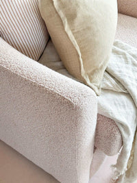 Close-up of norsu Studio Swivel Chair in blush boucle fabric with beige cushion and throw blanket