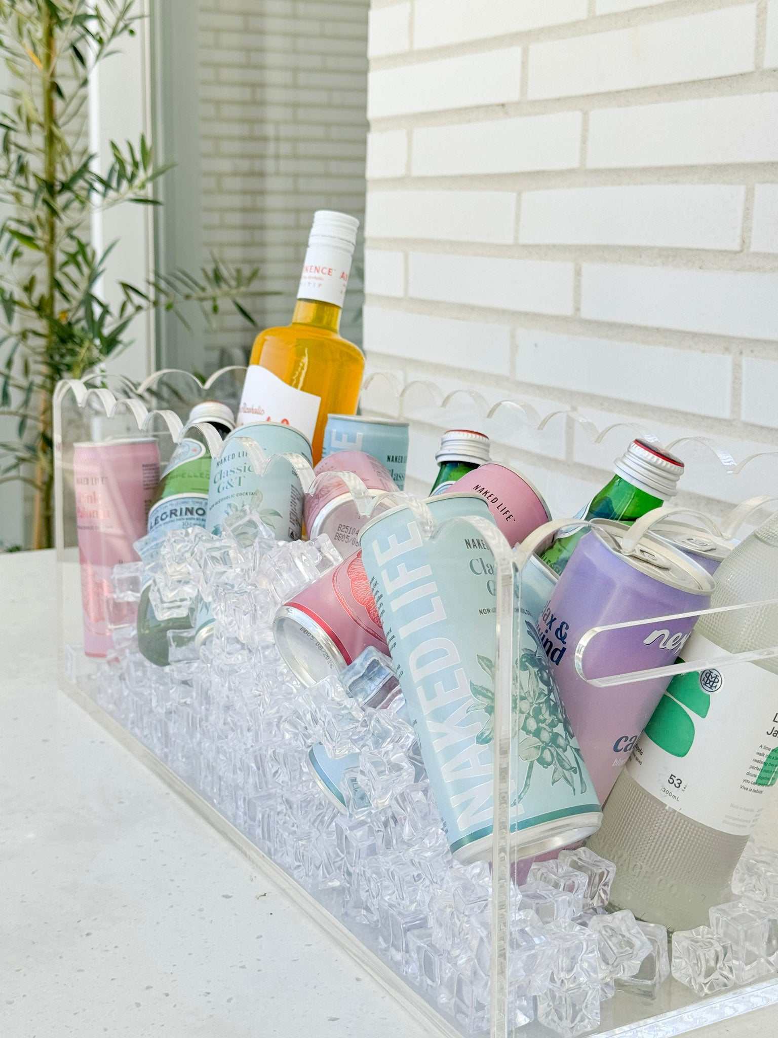 Clear Perspex scalloped drinks bucket filled with ice and assorted beverages on white surface