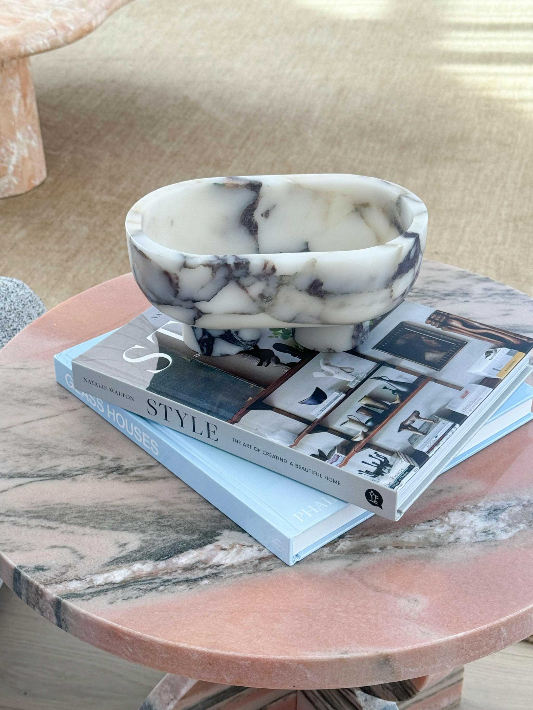 CoTheory marble footed oval tray in Viola marble with sculptural design and natural stone pattern placed on stacked books.