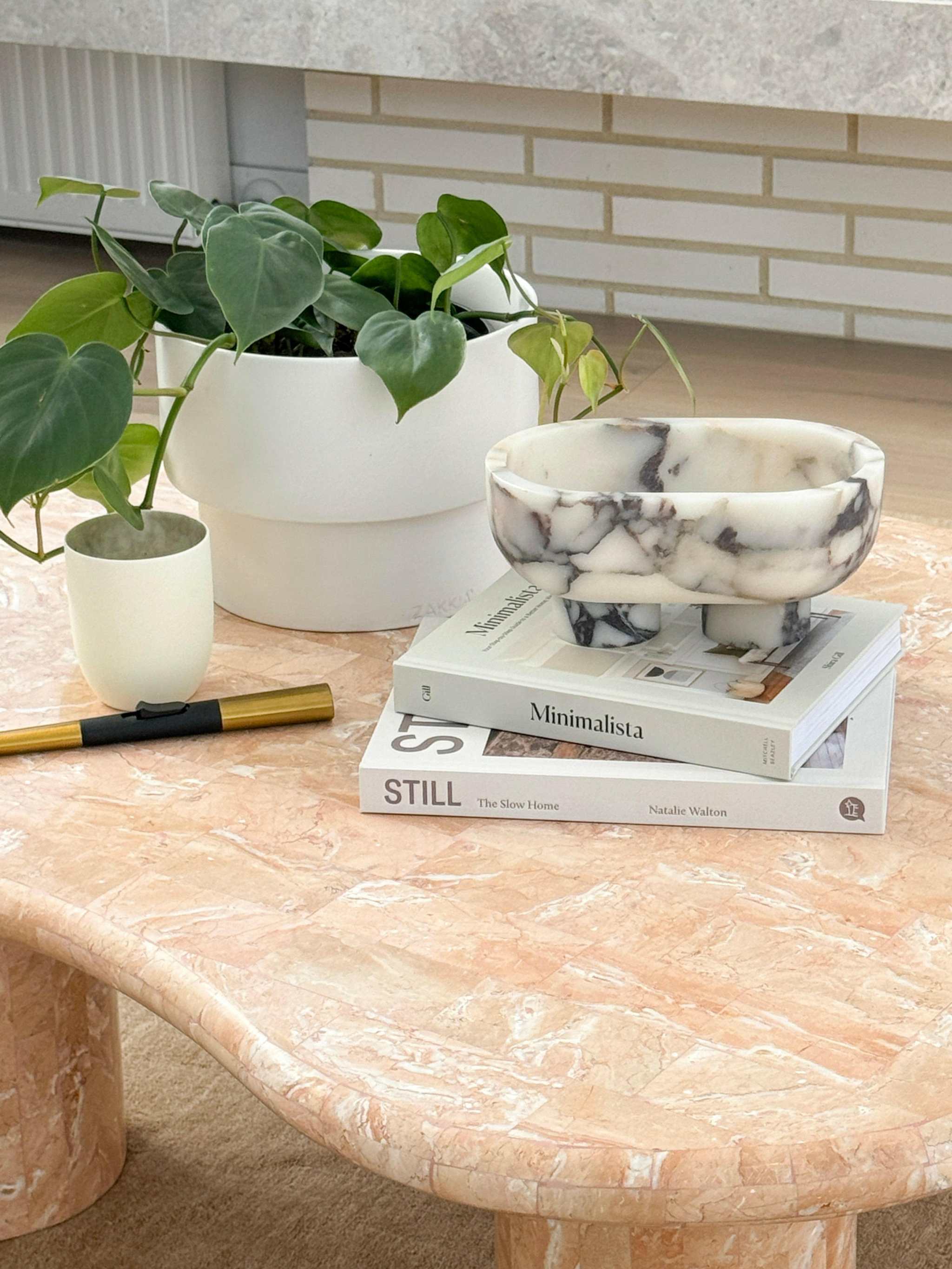 CoTheory Marble Footed Oval Tray in Viola Marble displayed on a marble table with decorative plants and books.