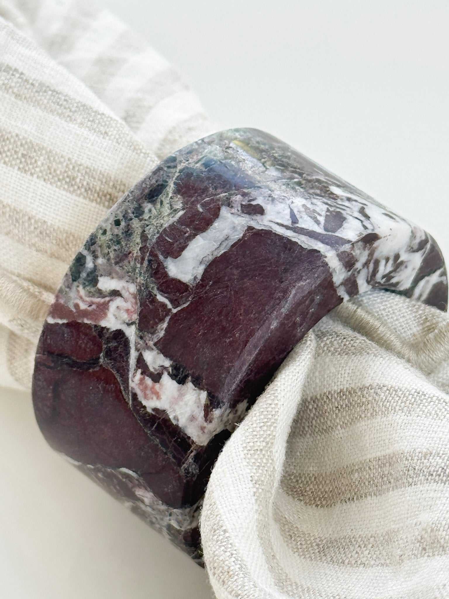 norsu STUDIO Marble Circular Napkin Ring in deep burgundy Rosso Levanto with white veining on striped linen napkin