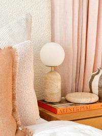 Cozy interior corner with textured pillows, a modern round lamp, and Arent & Pyke book on a wooden side table