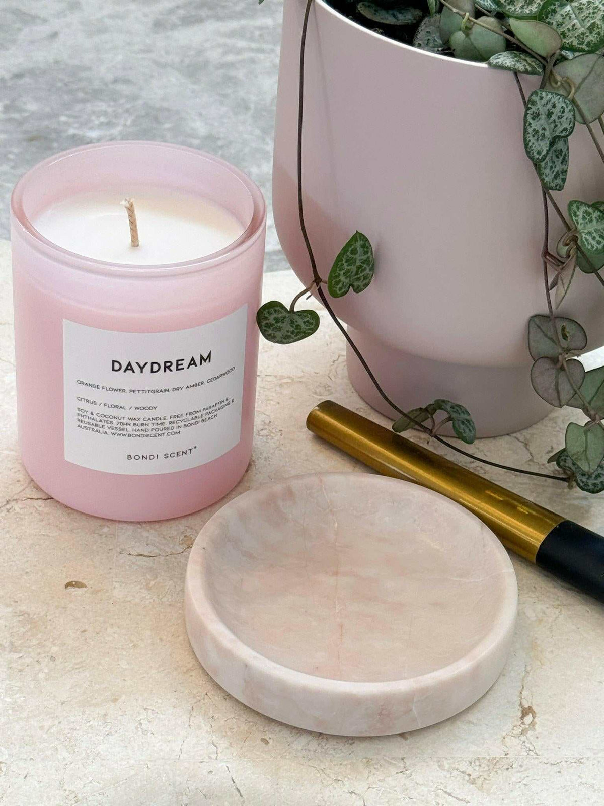 Bondi Scent Candle Daydream in pink jar with natural wax, fresh beachy fragrance, and marble lid near plant and pen