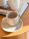 Robert Gordon Hand-Painted Mug in pastel tartan design with matching saucer on wooden table next to books