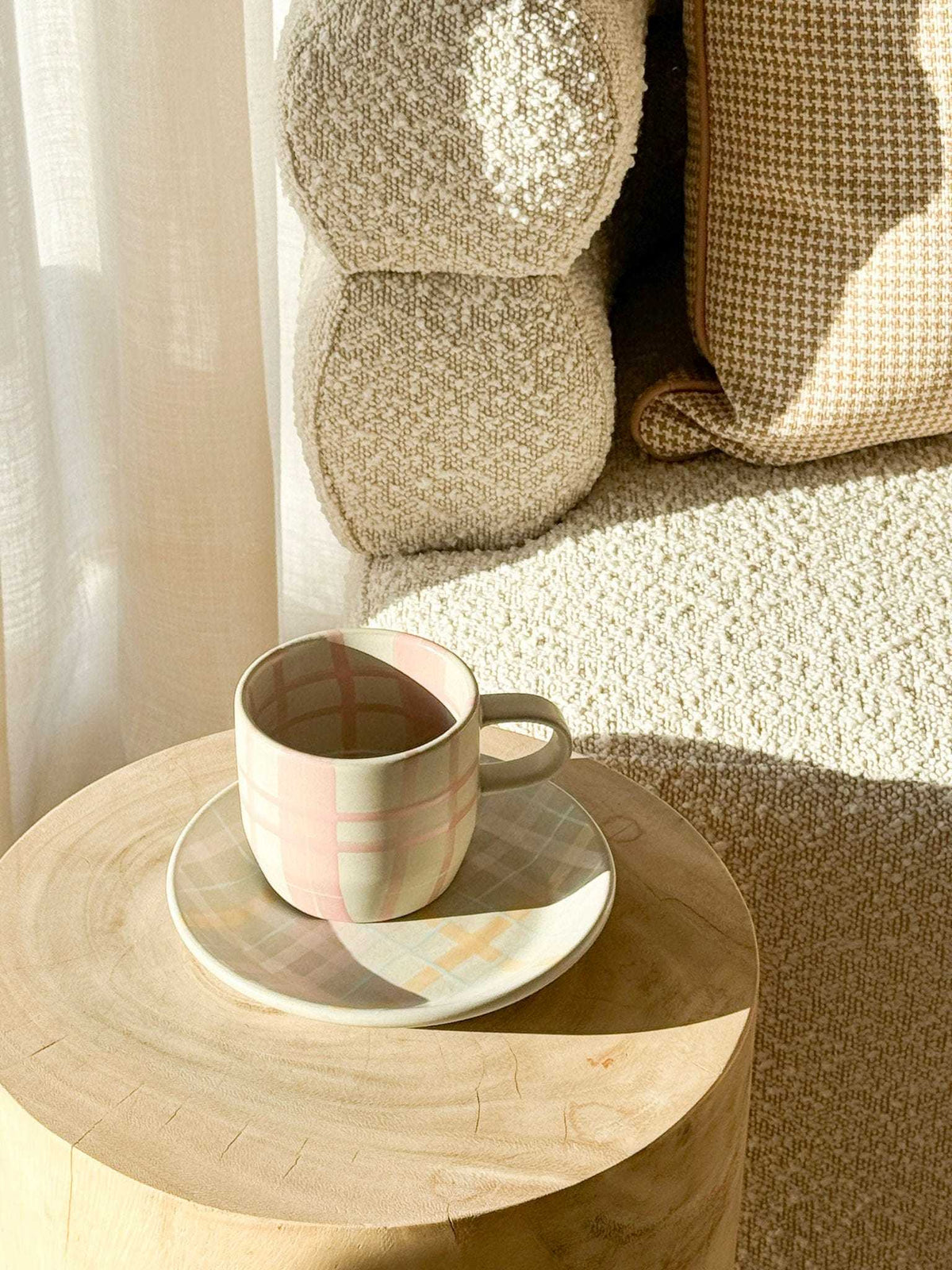 Robert Gordon hand-painted ceramic mug with plaid design on wooden table next to textured beige sofa