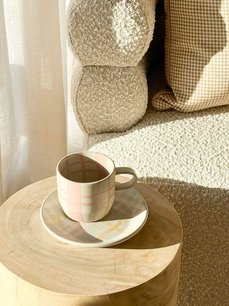 Robert Gordon hand-painted ceramic mug with plaid design on wooden table next to textured beige sofa