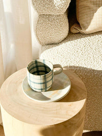 Robert Gordon Hand-Painted Mug with blue and white tartan design on wooden table in cozy living room setting