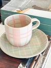 Robert Gordon hand-painted ceramic mug with pink tartan design and matching green checked saucer on books