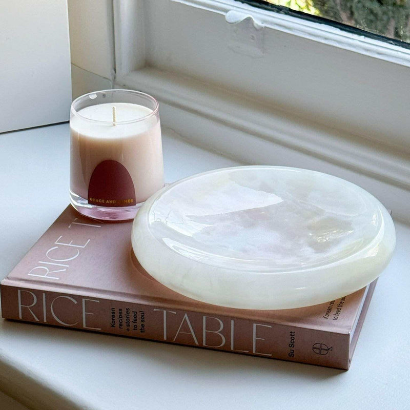 Small white CoTheory Onyx Tray Solstice with smooth curves placed on a book beside a candle.