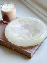 CoTheory Onyx Tray Solstice small white onyx sculpted tray with smooth curves on a book next to a candle