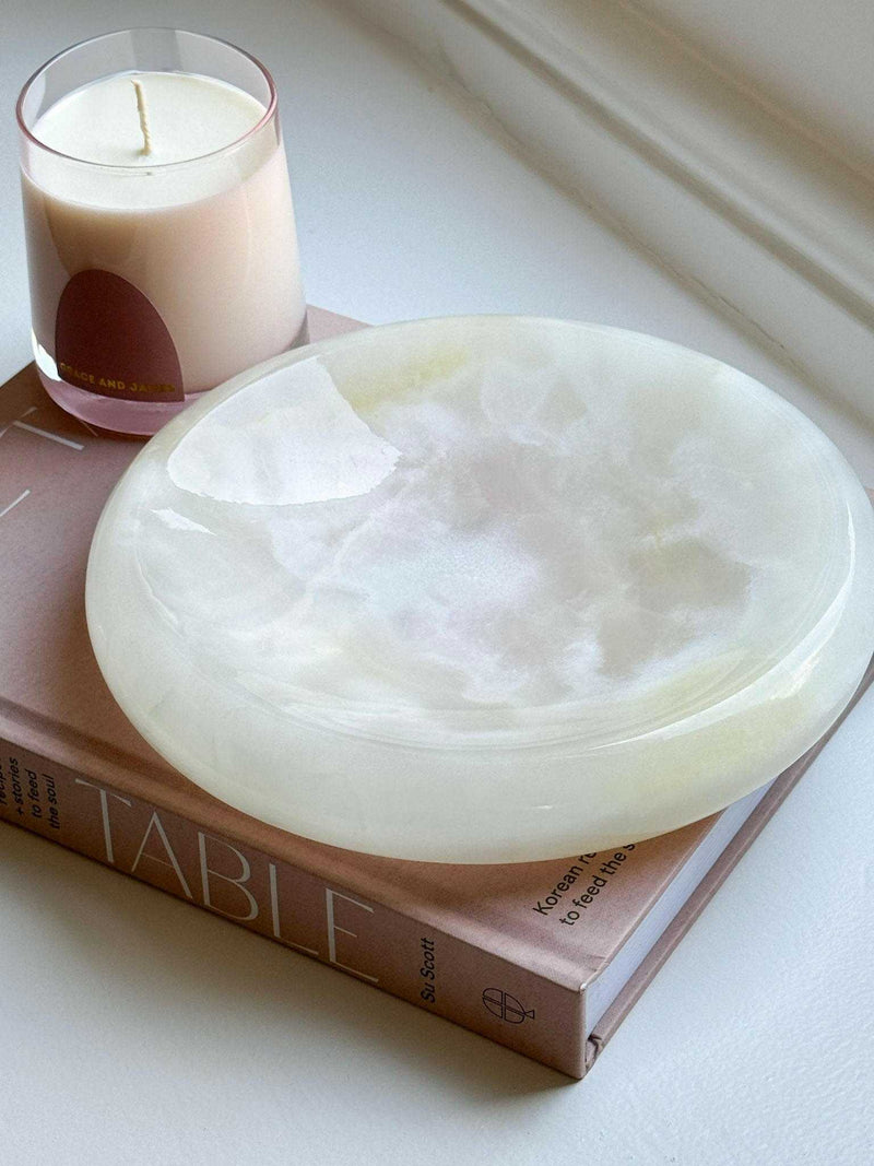 CoTheory Onyx Tray Solstice small white onyx sculpted tray with smooth curves on a book next to a candle