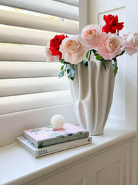 Small white onyx CoTheory Orbit Table Sculpture sphere displayed on stacked books next to a white vase with pink and red roses on a windowsill