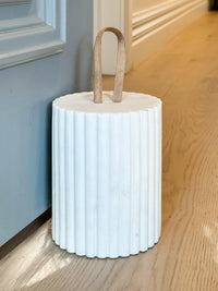 Isla Marble Doorstop white ribbed marble design with leather loop handle propping open door on wooden floor