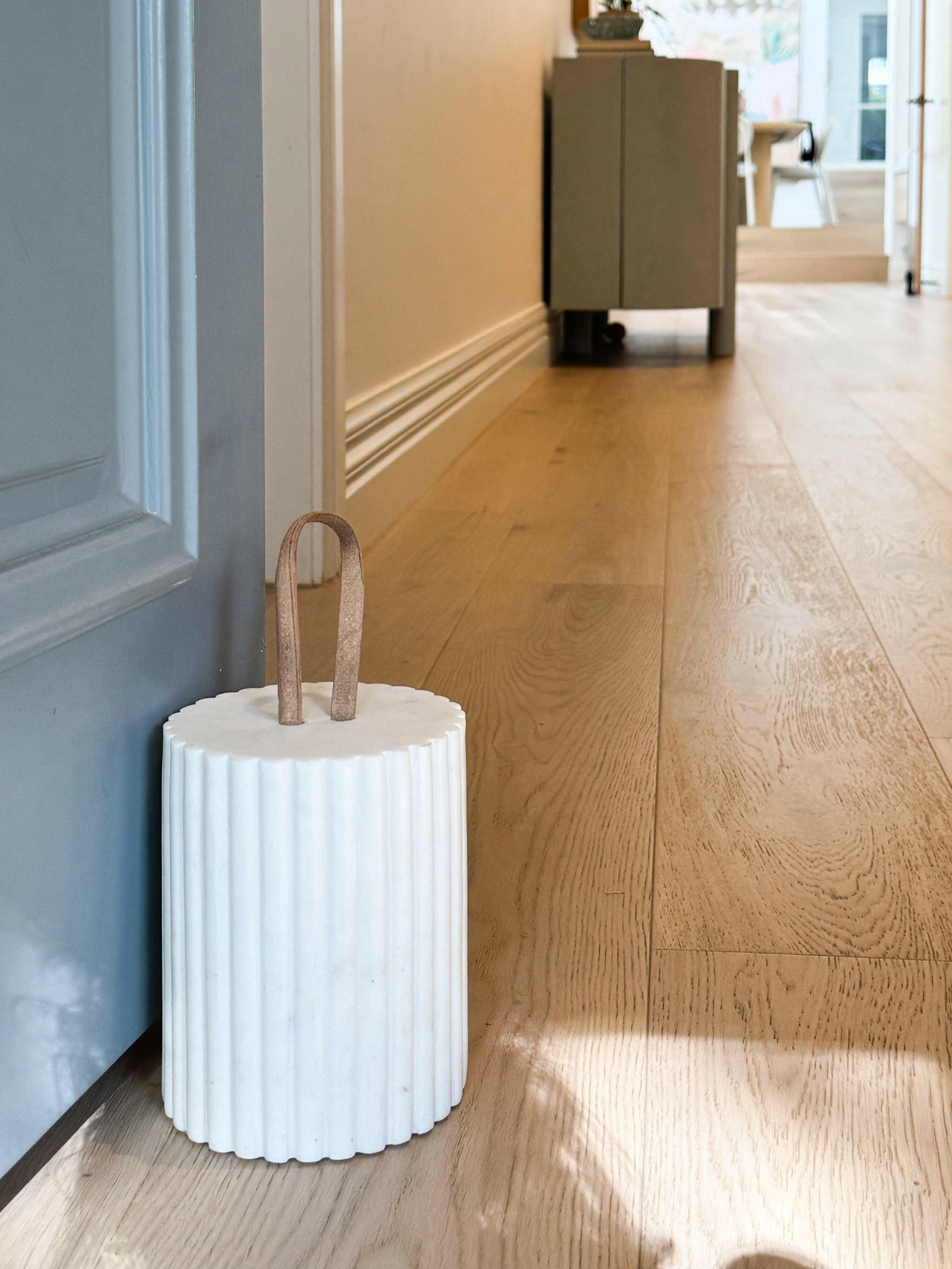 White ribbed Isla Marble Doorstop with leather handle on wooden floor holding door open in modern interior