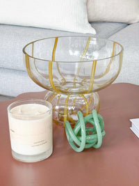 Clear Willow Glass Vase bowl with mustard-tone swirls on round base, styled on table with candle and decor.