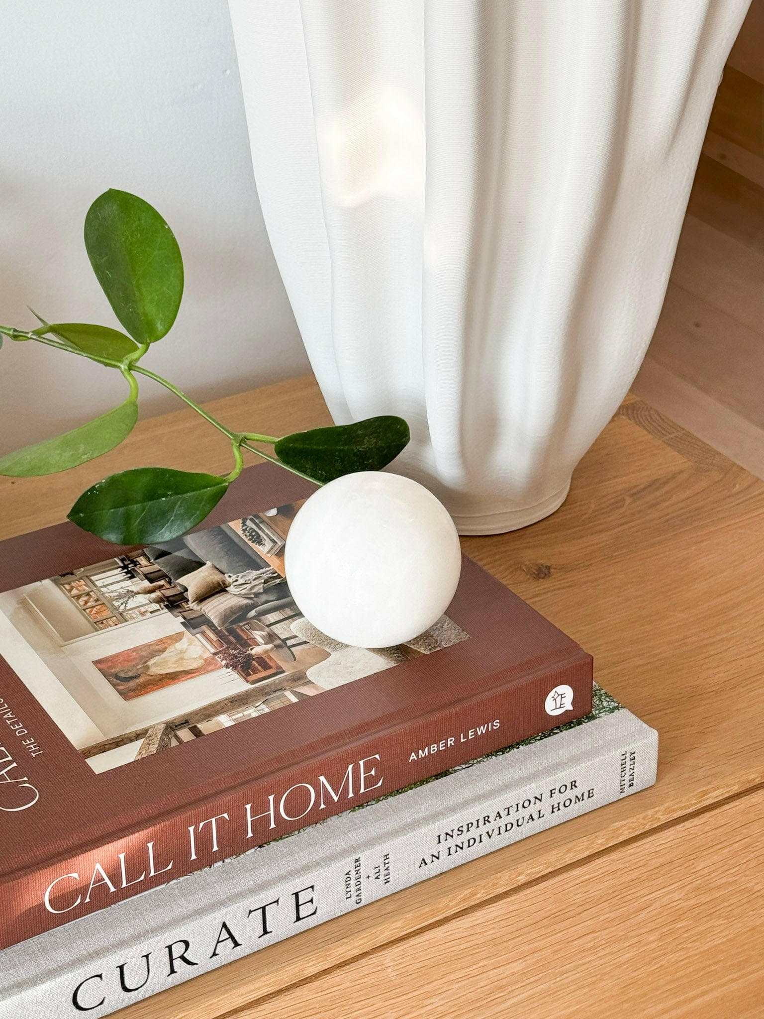 CoTheory Orbit Table Sculpture small white onyx sphere on books with plant and vase background